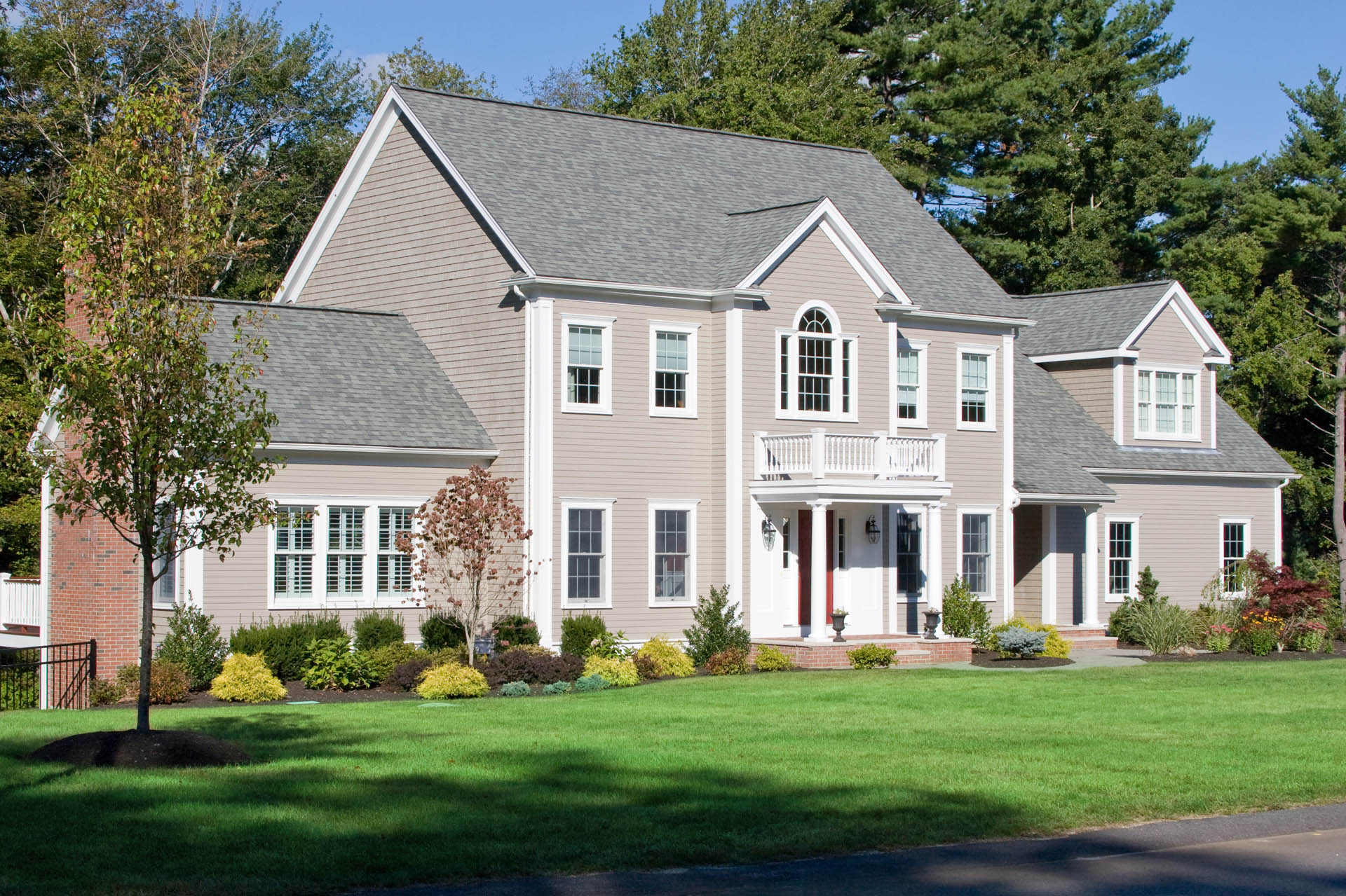 A large, suburban home with a grey shingle roof, grey siding, and a green lawn